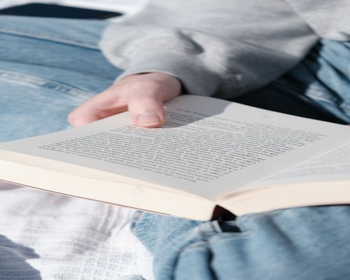 Person reading a physical book in bed with a small reading lamp