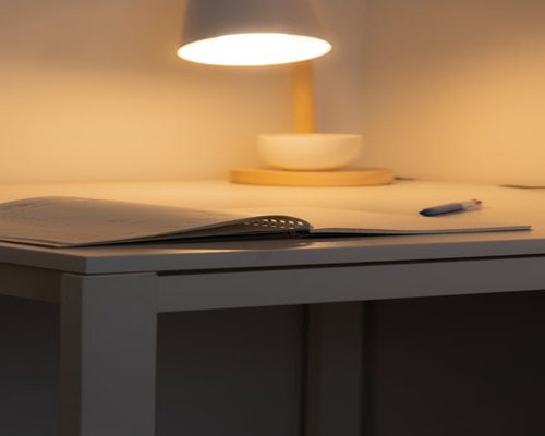Close up of a desk with a notebook, pen, and a warm desk lamp